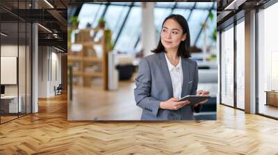 Young Asian business woman entrepreneur standing in office holding digital tablet. Businesswoman leader, professional company manager using smart corporate management technology looking at copy space. Wall mural