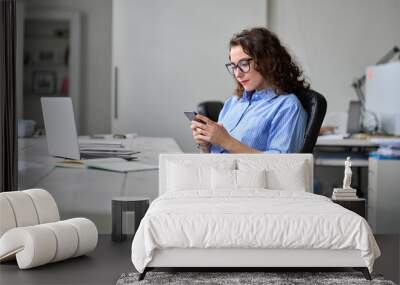 Young business woman entrepreneur looking at smartphone using cellphone mobile cell corporate tech, professional businesswoman manager working in office typing on mobile cell phone sitting at desk. Wall mural