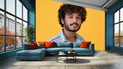 Young curly smart indian cool guy standing isolated on yellow background. Ethnic cool handsome man wearing denim shirt looking at camera posing for headshot close up face portrait. Wall mural