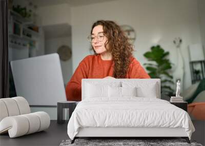 Young female student using laptop studying online, remote working at home office using laptop computer watching webinar, elearning web training, having work video call sitting at table, writing notes. Wall mural