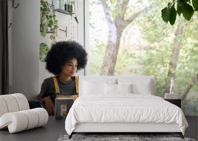 Young happy African American college student hipster girl with afro hair sitting at table in cafe indoor alone using laptop watching learning virtual online digital webinar. Wall mural