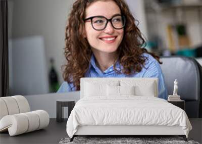 Young happy business woman company employee manager sitting at desk working on laptop. Pretty female professional worker using computer in corporate modern office looking away smiling. Vertical. Wall mural