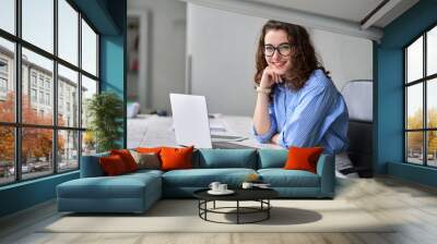 Young happy business woman company employee sitting at desk working on laptop. Smiling female professional entrepreneur worker using computer in corporate modern office looking at camera. Portrait. Wall mural