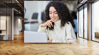 Young happy latin business woman company worker sitting in office working on laptop tech. Smiling female professional sales or marketing manager using corporate services on computer browsing internet. Wall mural