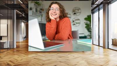 Young happy pretty business woman student sitting at desk at home office with laptop computer looking at camera advertising online learning, remote work, business webinars. Portrait. Wall mural