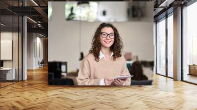 Young happy smiling professional business woman, female company worker or corporate manager holding digital tablet technology posing in modern office working, looking at camera, vertical. Wall mural