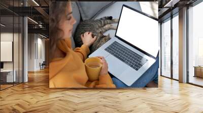 Young hispanic latin teen girl student relax sit on sofa with cat holding laptop looking at mock up white computer screen online learning on pc, elearning, watching movie. Over shoulder closeup view Wall mural