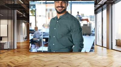 Young Latin business man looking at camera in office, vertical portrait. Smiling happy businessman, male executive manager, professional employee or worker looking at camera standing at work. Wall mural