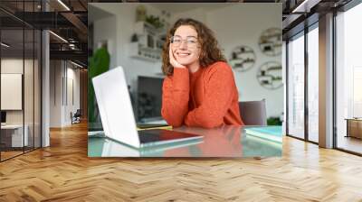 Young smiling pretty business woman student sitting at table at home office with laptop computer looking at camera advertising elearning online course, remote work, business webinar. Portrait. Wall mural