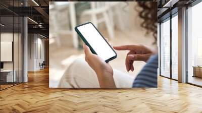 Young woman user holding smart phone in hand touching finger mock up white empty cellphone screen using mobile applications at home. Display mockup close up over shoulder view. Wall mural