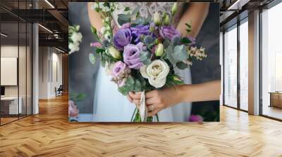 A close-up of a bride holding a beautiful bridal bouquet with purple and white flowers. The bouquet is made up of various flowers, including roses, lilies, and greenery. Wall mural