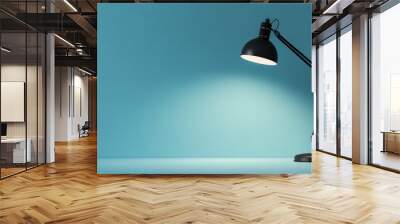 A black desk lamp shining directly on a blue wall, creating a focused, minimalist lighting effect with soft, calming tones. Wall mural