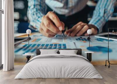 Investor or financial professional closely examining various charts,graphs,and reports on a desk They appear to be analyzing data and considering different investment options Wall mural