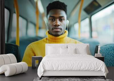 Portrait of a young African American man sitting on a city bus wearing earbuds and intently focused on watching something on his smartphone device while commuting to work or his destination Wall mural