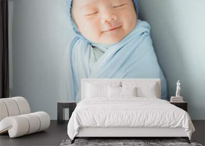 An adorable cute smiling Asian newborn baby with blue knitted hat and wrapprd in cocoon sleeping on bed Wall mural