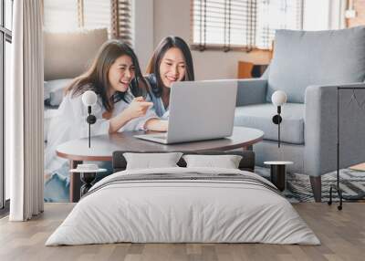 Two happy Asian women laughing while working with laptop at home Wall mural