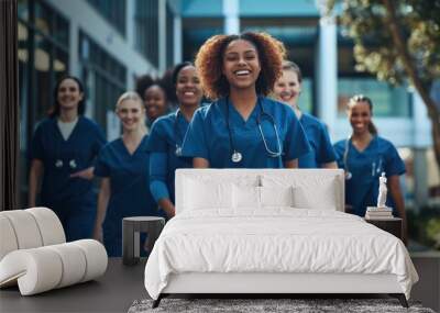 A diverse group of smiling female student nurses wearing blue scrubs walks together outside a medical school on a university hospital campus. Wall mural