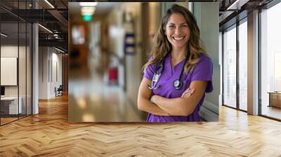 Female nurse in scrubs smiling with arms crossed, portrait of a beautiful young woman doctor wearing a purple uniform and stethoscope working on a hospital background. Wall mural