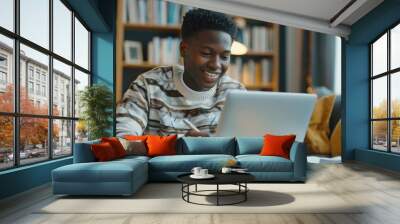 Portrait of teenage black boy using laptop computer at home. A teenage boy attending to online school class Wall mural