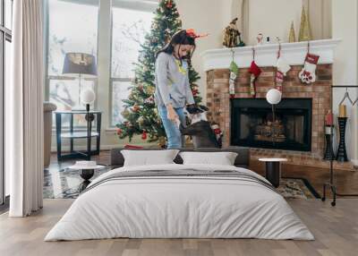 Girl dancing with her pet dog in front of Christmas tree and fireplace Wall mural