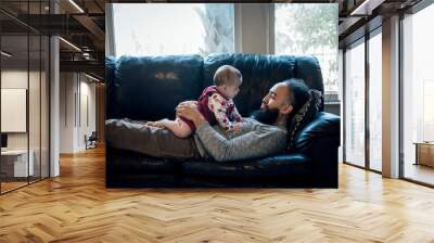 Man relaxing on couch playing with baby on his chest Wall mural