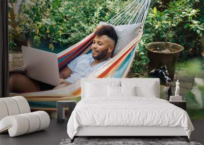 Man working from home on laptop computer while relaxing in hammock in the back yard Wall mural