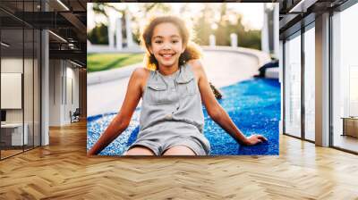 Portrait of smiling tween girl sitting in park at sunset Wall mural