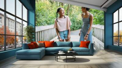 Teen girls walking and laughing together on bridge in nature park Wall mural