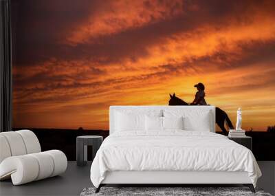 A rider and a horse silhouette at sunset; a cowgirl riding on his horse with a dramatic sunset in the background; western lifestyle; portrait photography Wall mural