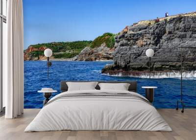 Two people on the edge of a high cliff above the sea in the abandoned Emirgan Ulas Mesire Yeri Park in Alanya (Turkey). Seascape with natural gray layered granite wall on the shore Wall mural