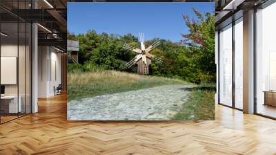 Ukraine, Pyrohiv (Kiev) - September 17, 2017: A wooden antique windmill stands near a forest and a paved road in the Museum of Folk Architecture and Life Wall mural