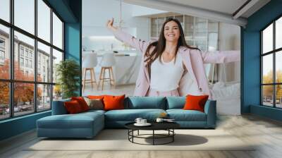 Grateful young businesswoman in light pink suit spreading hands toothy smiles wants to hug looks at camera. Brunette Korean successful student girl enjoying apartment. Tanned female relaxing home. Wall mural