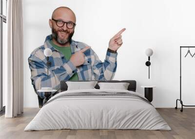 Positive Caucasian bald beardy man in plaid shirt pointing any index finger at empty space looks at camera against transparent background. Excited Italian male in glasses, teacher. Mockup, promo. Wall mural