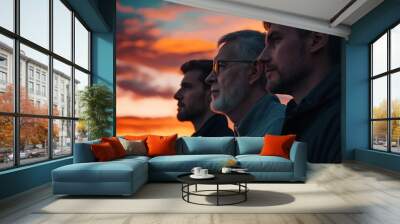 Three men of varying ages stand together, gazing thoughtfully ahead, against a vibrant sunset sky, embodying wisdom and unity. Wall mural