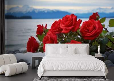 Vibrant red roses dot the foreground as waves crash on a pebbled shore, with a distant view of mountains under a cloudy sky. Wall mural