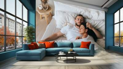 Young caucasian sleeping couple in bed. Handsome beardy European man laying with wife at bedroom enjoying Sunday morning. Calm hispanic young adult woman having nap at hotel with husband. Wall mural