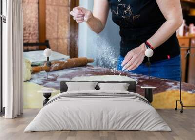 Housewife sprinkling flour on the dough on kitchen table Wall mural