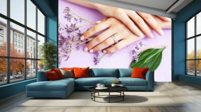 pretty perfect woman hands with white manicure and little flowers on colorful lilac background, green leaf spa concept Wall mural