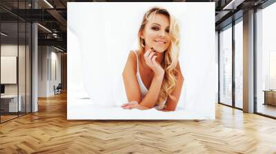 young pretty blond woman in bed covered white sheets smiling che Wall mural