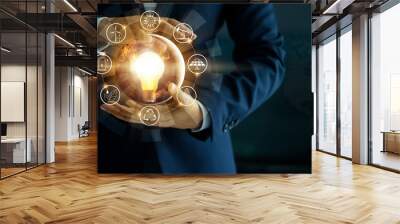 Businessman' s hand holding glowing light bulb with energy sources icon. Campaigning for ecological friendly and sustainable environment.  Wall mural