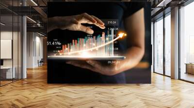 Businessman holding tablet and showing a growing virtual hologram of statistics, graph and chart with arrow up on dark background. Stock market. Business growth, planing and strategy concept. Wall mural