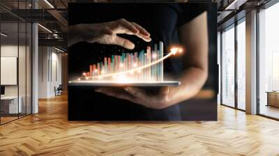 Businessman holding tablet and showing a growing virtual hologram of statistics, graph and chart with arrow up on dark background. Stock market. Business growth, planing and strategy concept. Wall mural