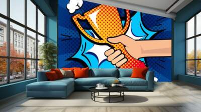 Hand holding gold trophy. We are the champions banner in pop art style. Trophy cup on burst background. Vector illustration Wall mural