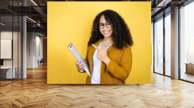 African american business woman with paperwork in hands over yellow background amazed and pointing with hand and finger Wall mural