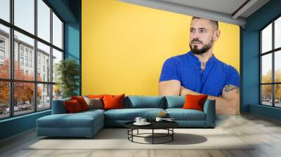 Handsome man with beard wearing blue polo shirt over yellow background looking to the side with arms crossed convinced and confident Wall mural