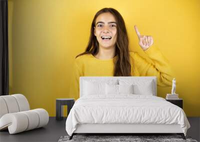 Pretty girl wearing a yellow sweater standing over isolated yellow background having an idea Wall mural