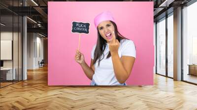 woman wearing pink headscarf over isolated pink background holding blackboard with fuck cancer word message showing middle finger doing fuck you bad expression and rude attitude. screaming excited Wall mural