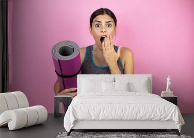 Young beautiful woman wearing sportswear over isolated pink background with her hand over her mouth and surprised. Holding a splinter in her hand. Wall mural