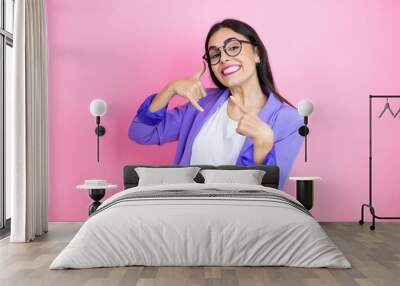 Young business woman wearing purple jacket over pink background doing the “call me” gesture with her hands. Wall mural