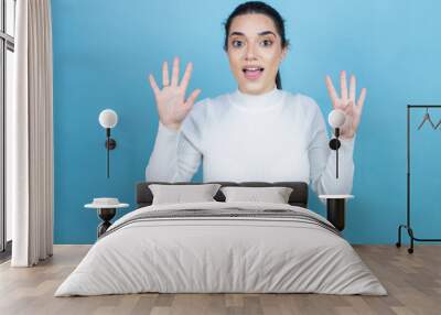 Young caucasian woman wearing white sweater over blue background showing and pointing up with fingers number nine while smiling confident and happy Wall mural